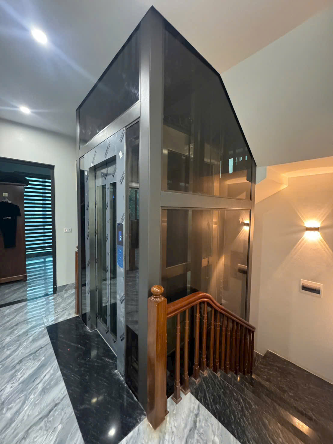 Thang máy gia đình vách kính khung inox lắp cạnh cầu thang trong nhà sang trọng
